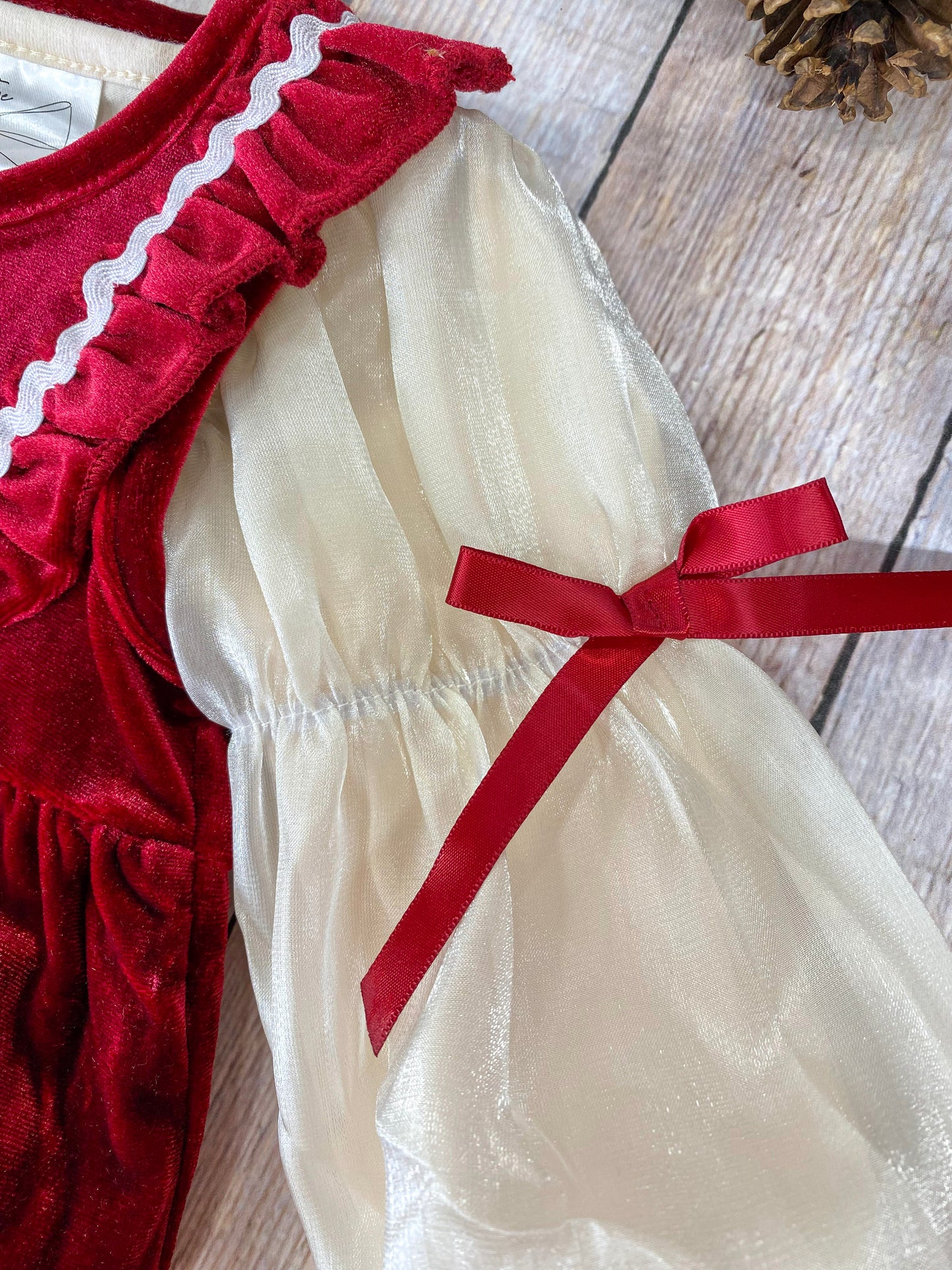 Close-up view of the romper's sleeve, showing the sheer cream fabric with a delicate shimmer. The sleeve is puffed and gathered at the wrist, tied with a small red velvet ribbon for a festive touch.