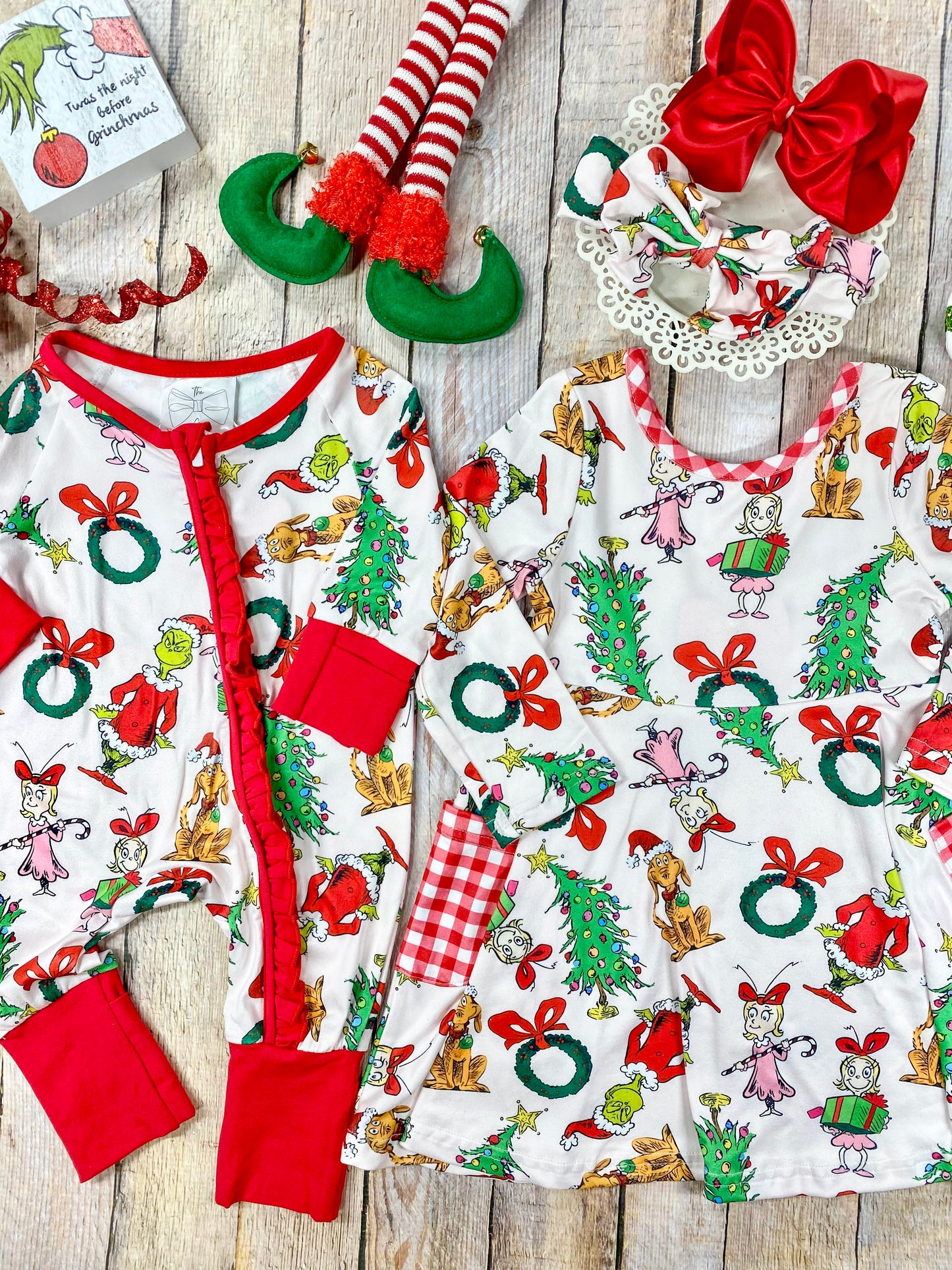 Matching Grinch-themed baby romper and girls’ long sleeve twirl dress featuring a white background with colorful all-over prints of classic Dr. Seuss Grinch characters, red bows, wreaths, and Christmas trees. The romper has red trim, cuffs, and a front ruffle zip closure, while the dress includes red and white gingham side pockets and a scoop neckline.