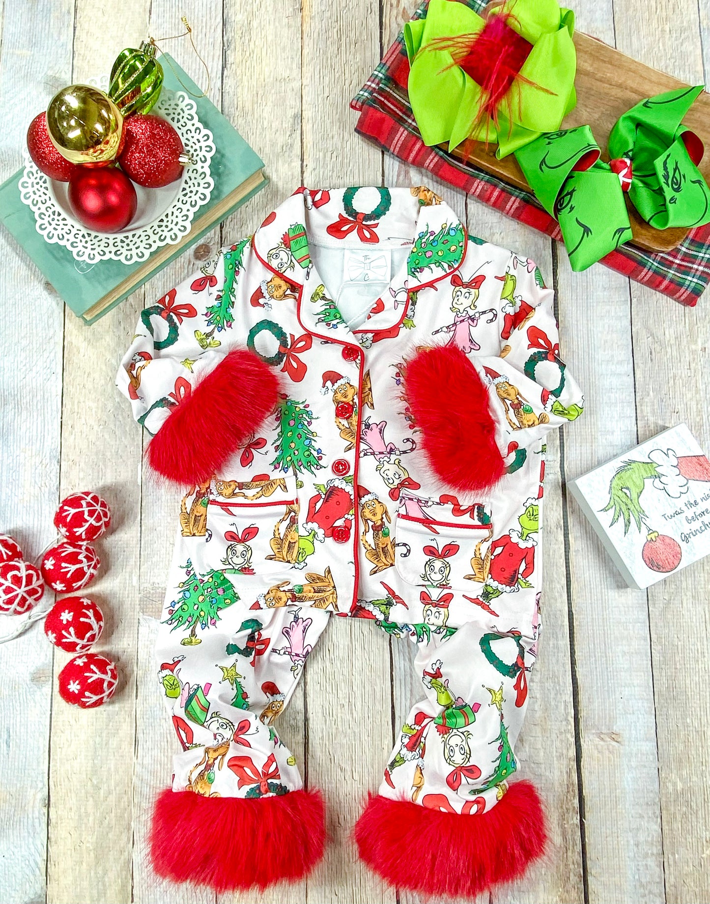 Girls’ festive Grinchmas pajama set with white background and colorful holiday print. Includes a button-up collared top and matching pants, both trimmed with plush red faux fur on sleeves and cuffs—perfect for Christmas morning photos.