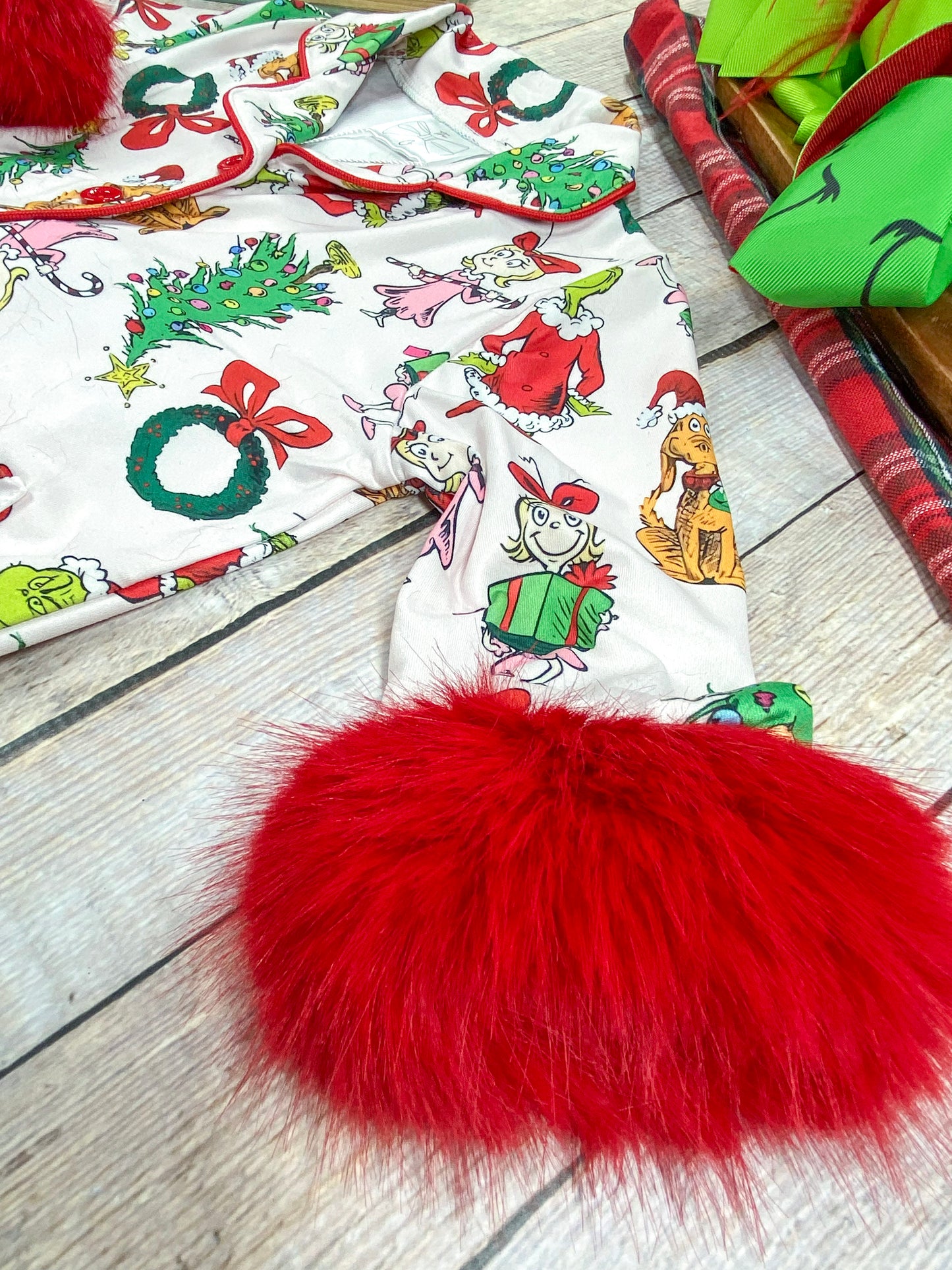 Detailed close-up of a long pajama sleeve in white fabric with colorful Grinch-themed print, featuring a vibrant red faux fur cuff that adds a cozy, festive touch and soft texture for extra warmth.