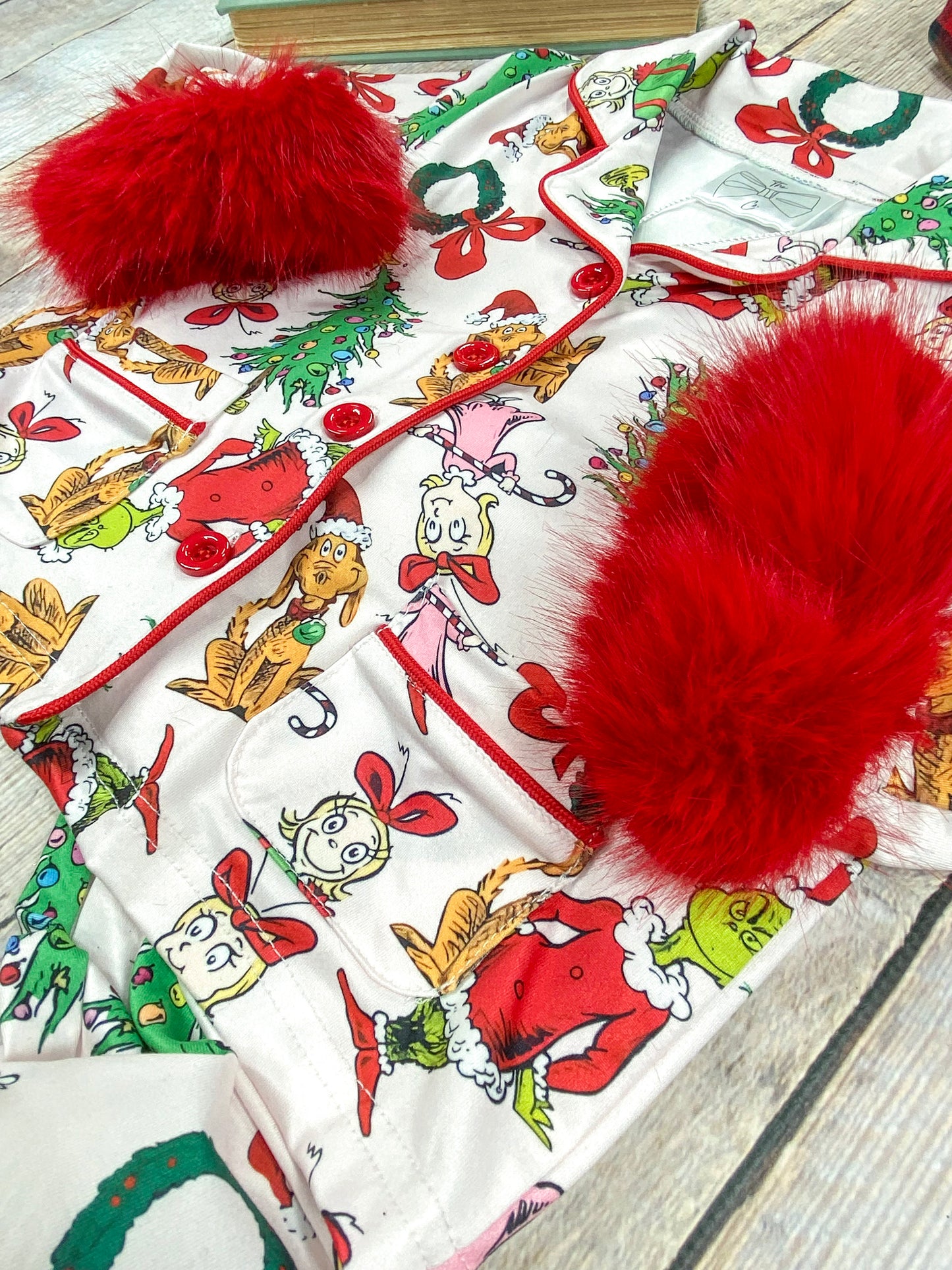 Detailed close-up of white pajama fabric featuring colorful Christmas-themed Grinch characters including the Grinch, Max the dog, Cindy Lou Who, decorated Christmas trees, red bows, and wreaths.