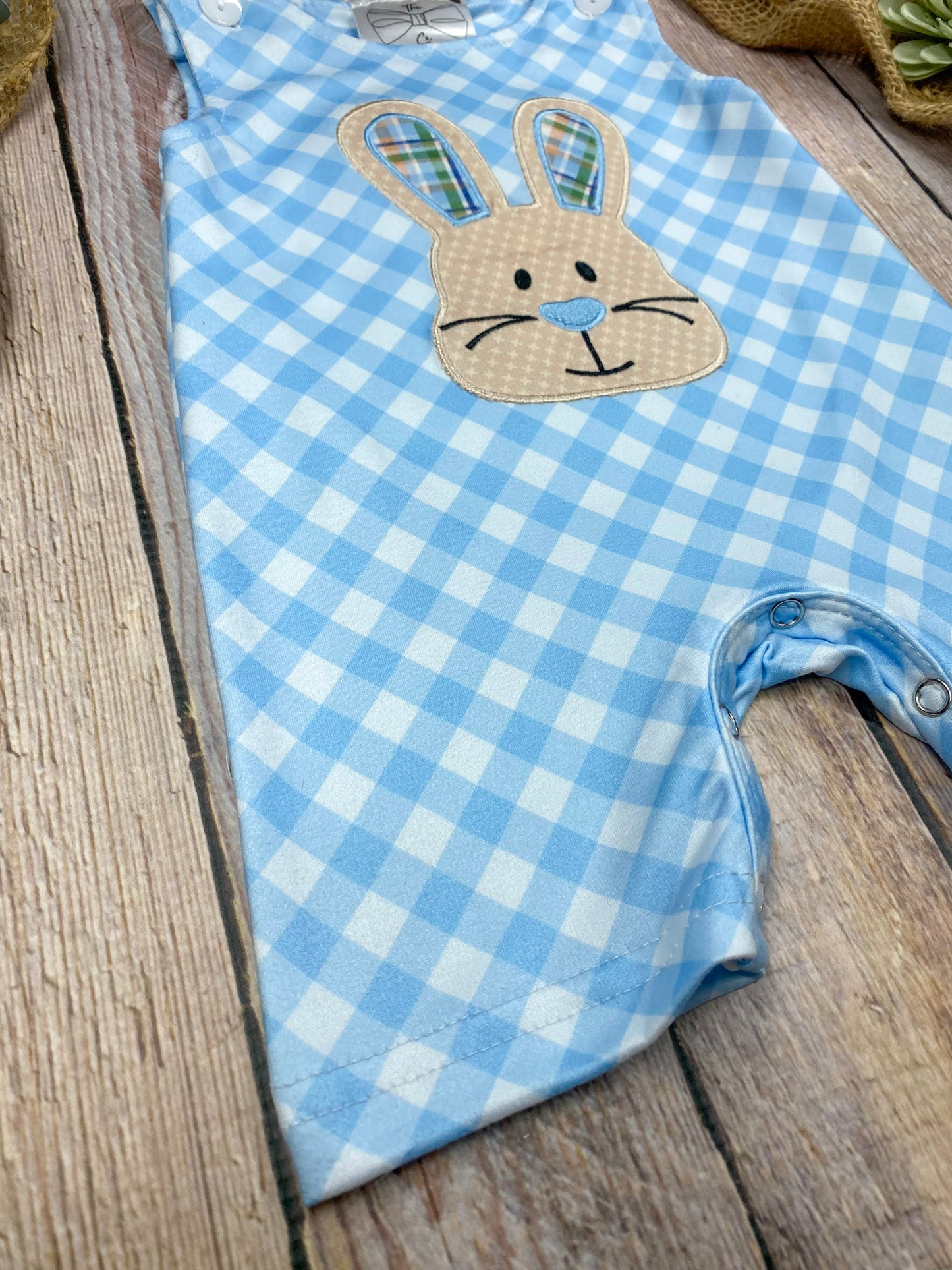 Blue checkered baby romper with a bunny face on a wooden surface