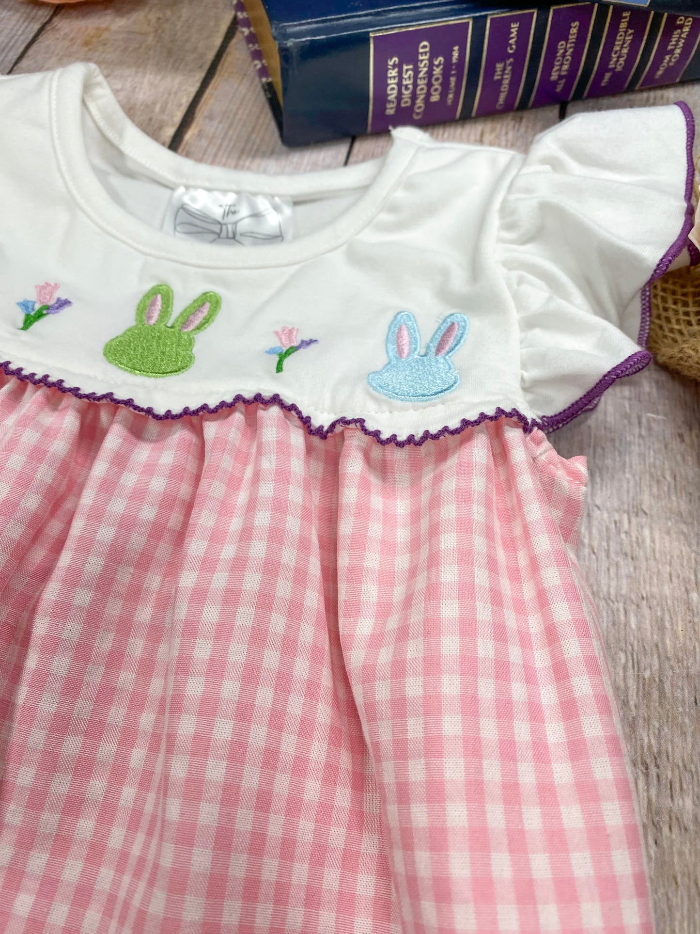 Pink checkered dress with embroidered bunny designs on a wooden surface