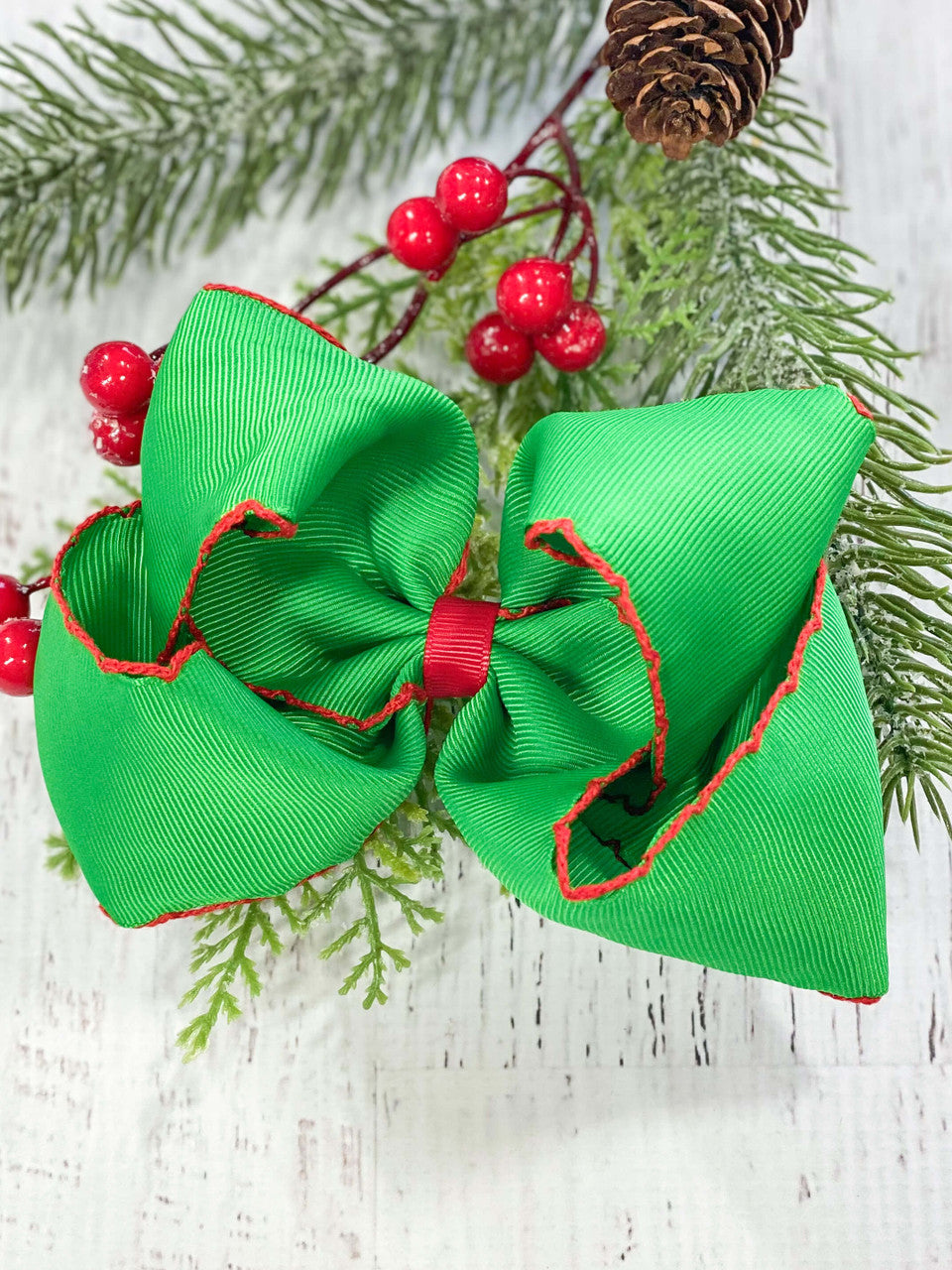 Emerald green hair bow with red center and red outline stitching.