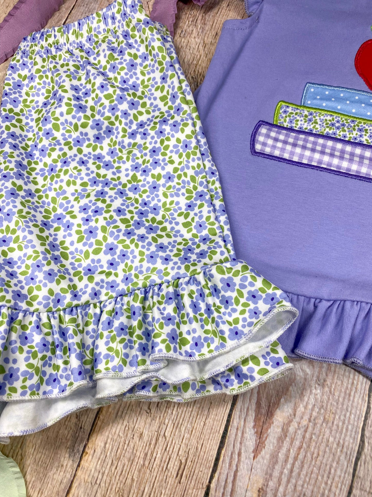Children's outfit with purple top and floral shorts on a wooden background