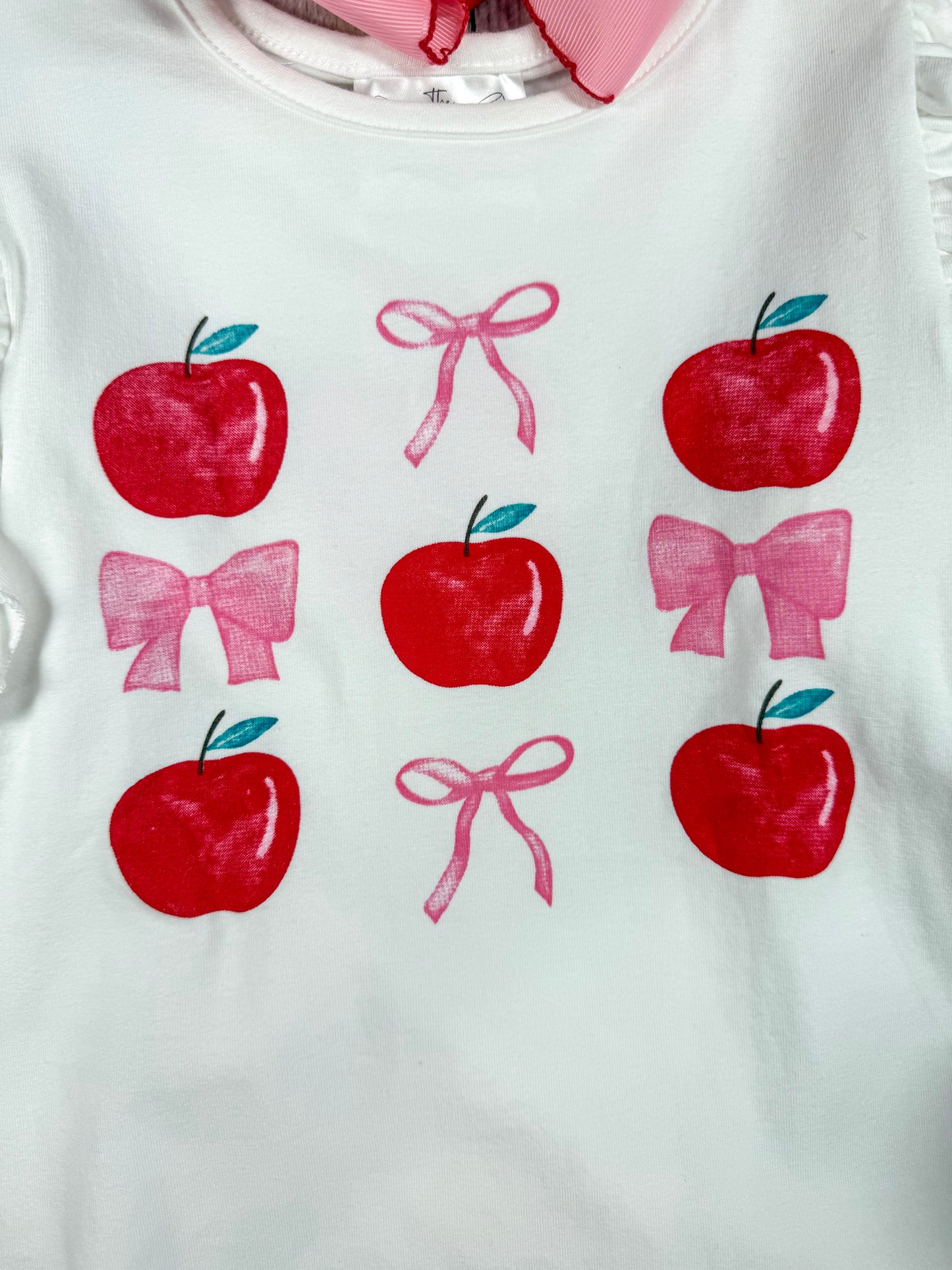 close up photo showing the apples and bows in a tic-tac-toe fashion on front of the shirt