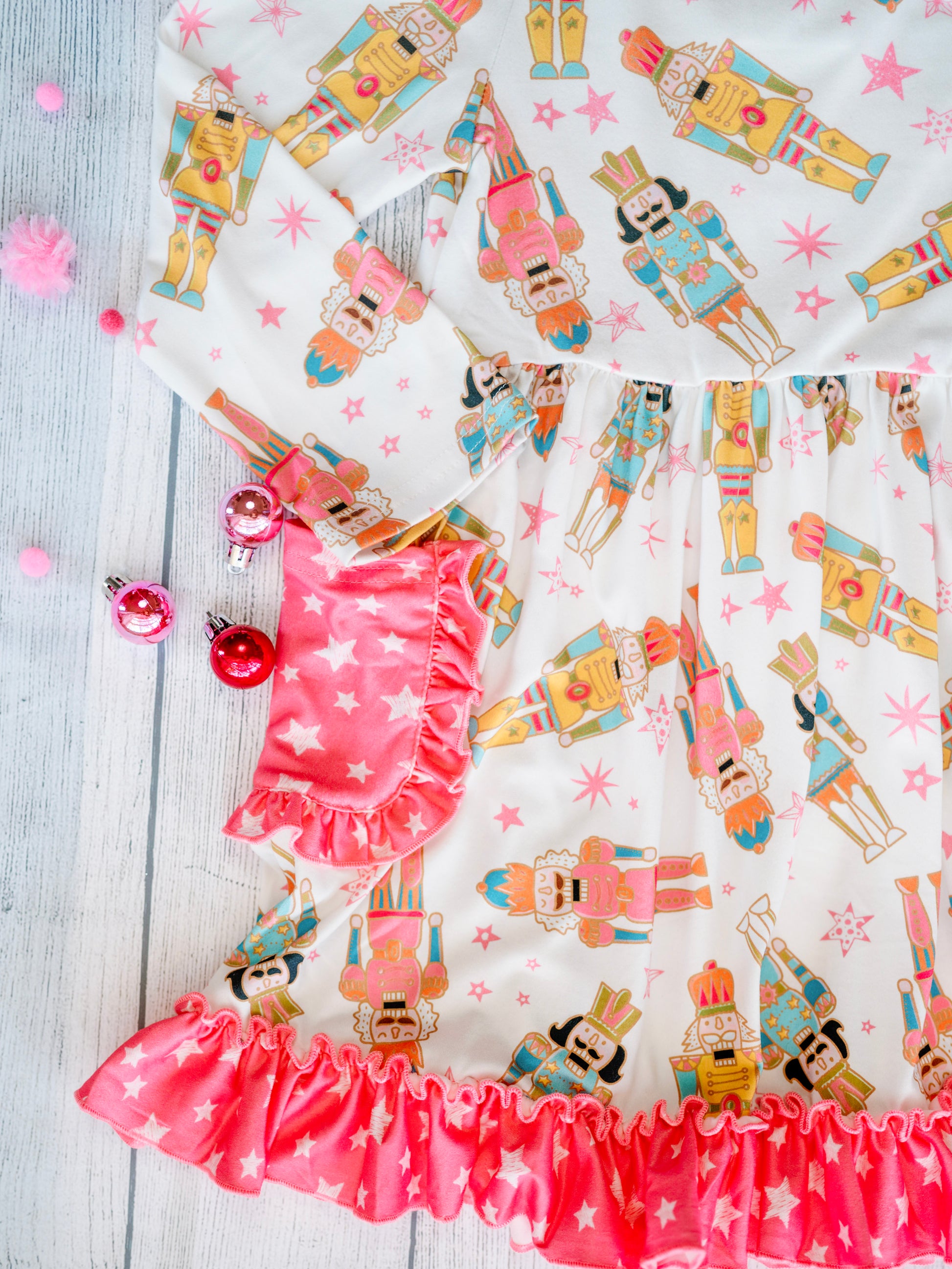 Close-up of the Nutcracker Galore Twirl Dress with Pockets, featuring a colorful nutcracker print on white fabric with pink star accents. The dress includes pink star-patterned side pockets with ruffled trim and a coordinating ruffle hem along the skirt.