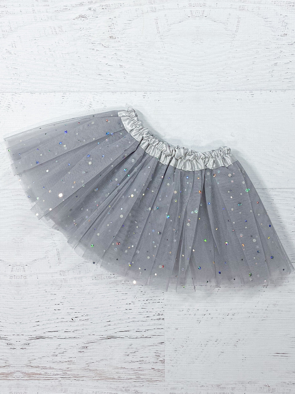 This soft grey tutu is made from polyester tulle, with a silver satin elastic waistband. The top of three layers is covered with silver sparkle dots in varying sizes.