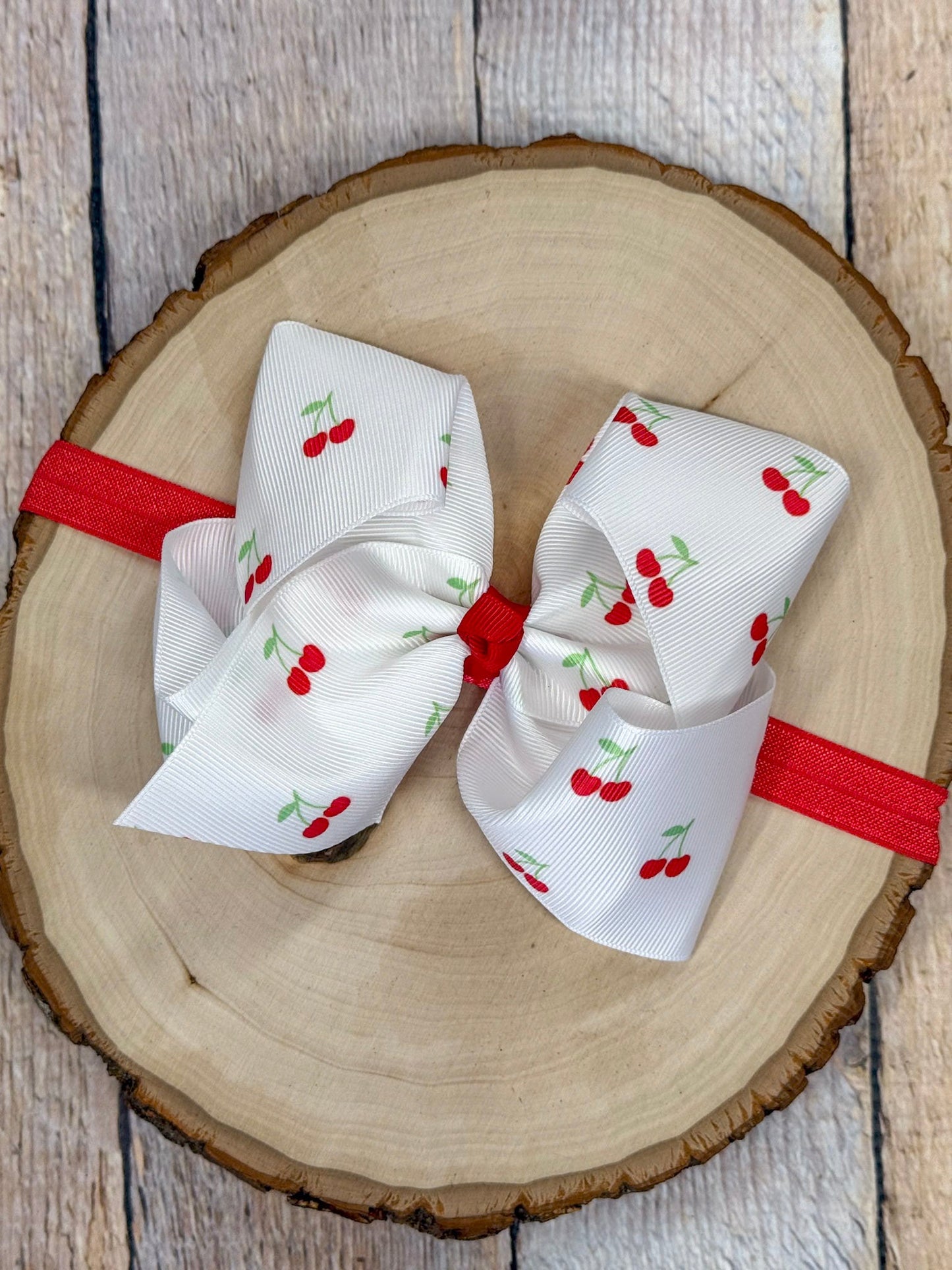 Cherry print bow attached to red elastic headband for babies and toddlers