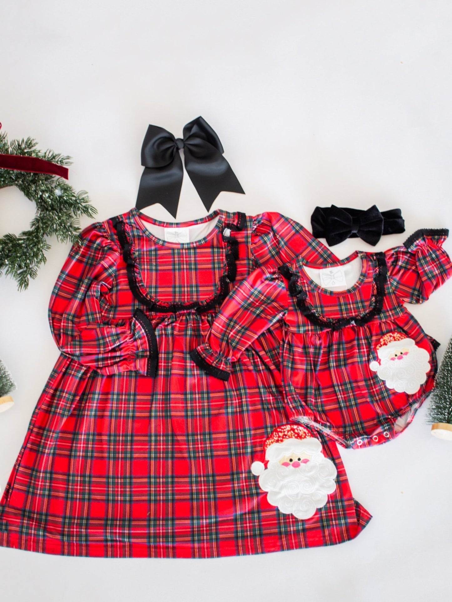 Red plaid dress with black trim and Santa Claus design, accompanied by black bows on a white background.