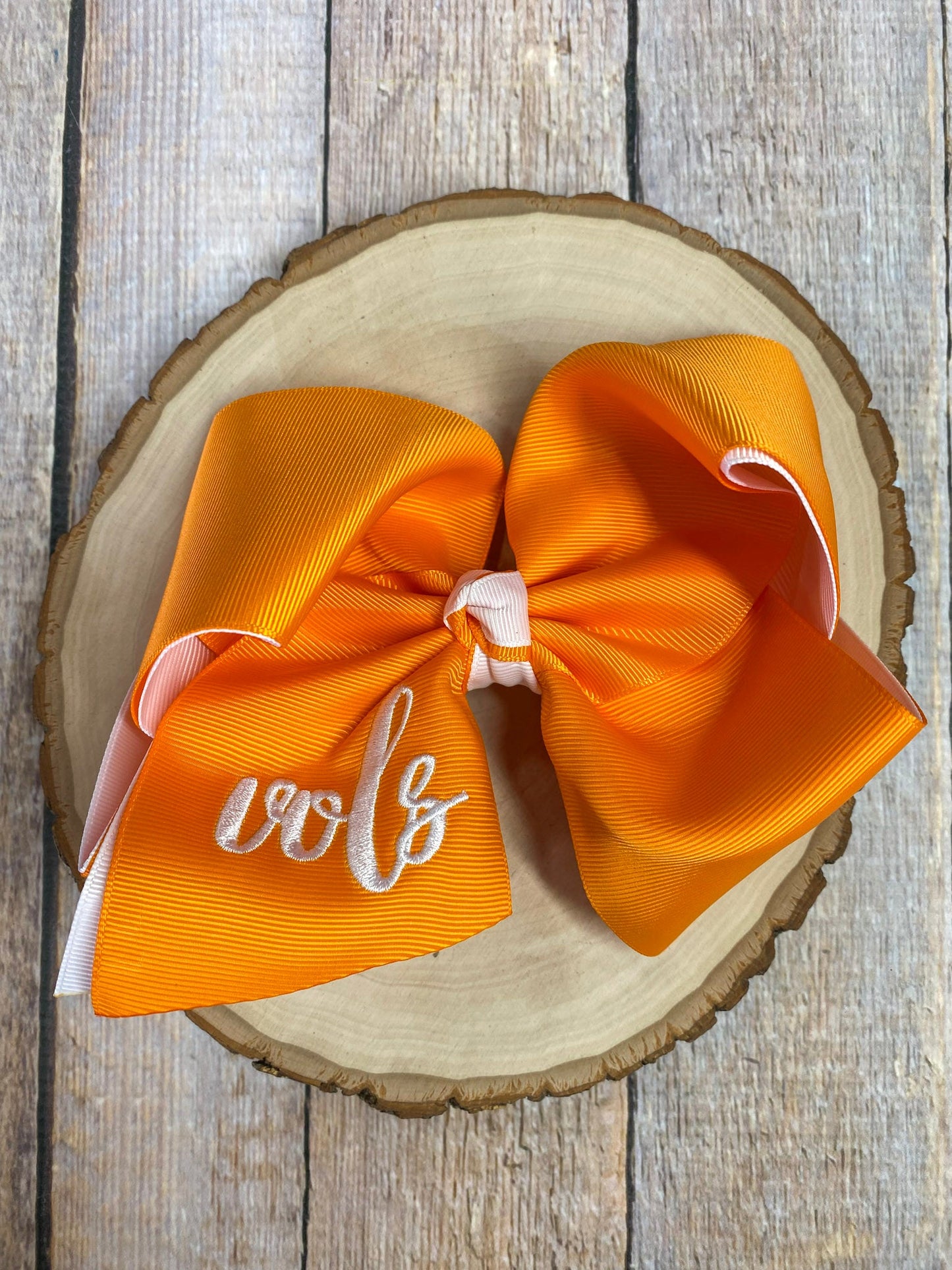 Orange hair bow with white lettering on a wooden surface