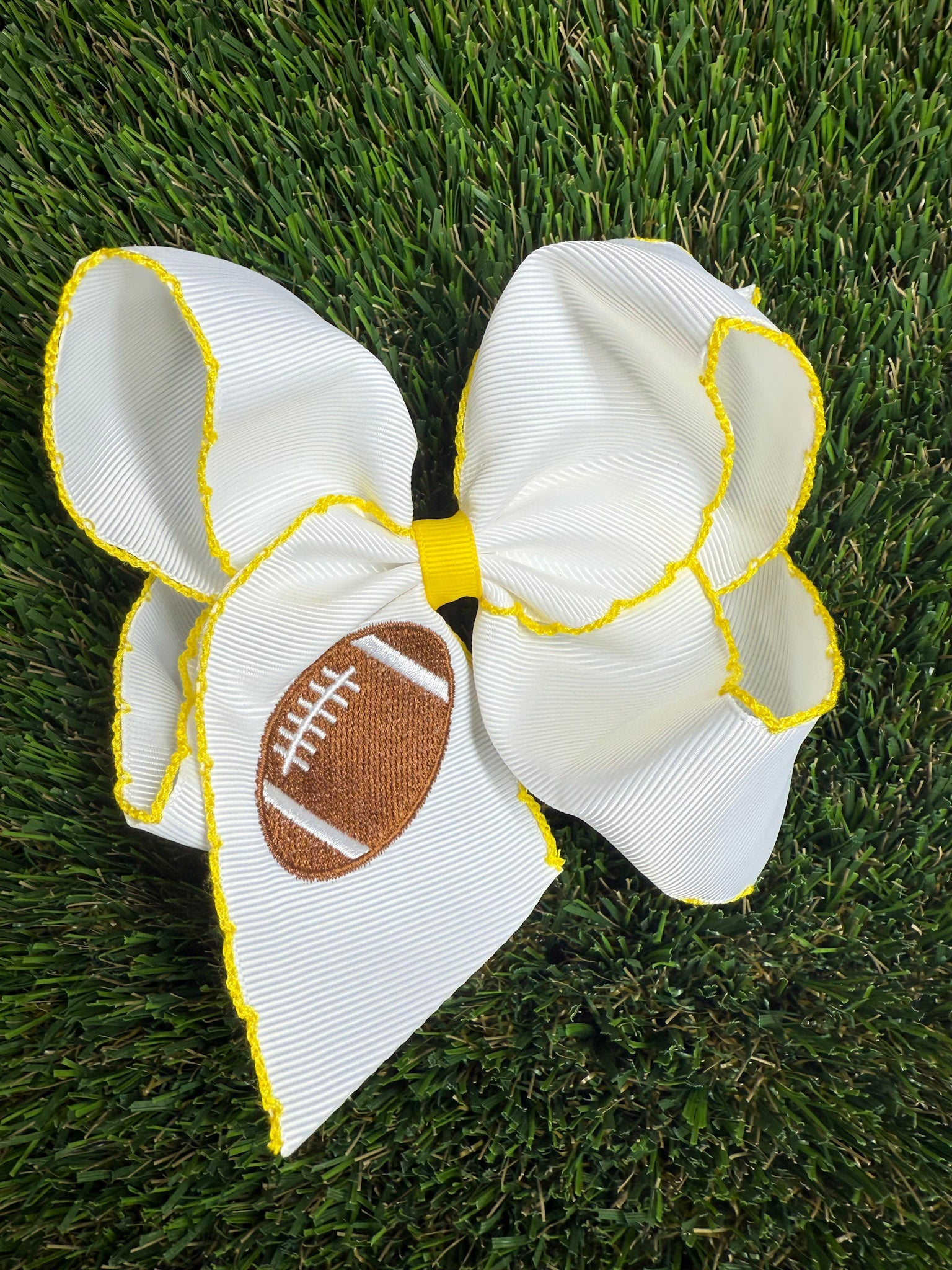 White bow with yellow trim and a football design on grass