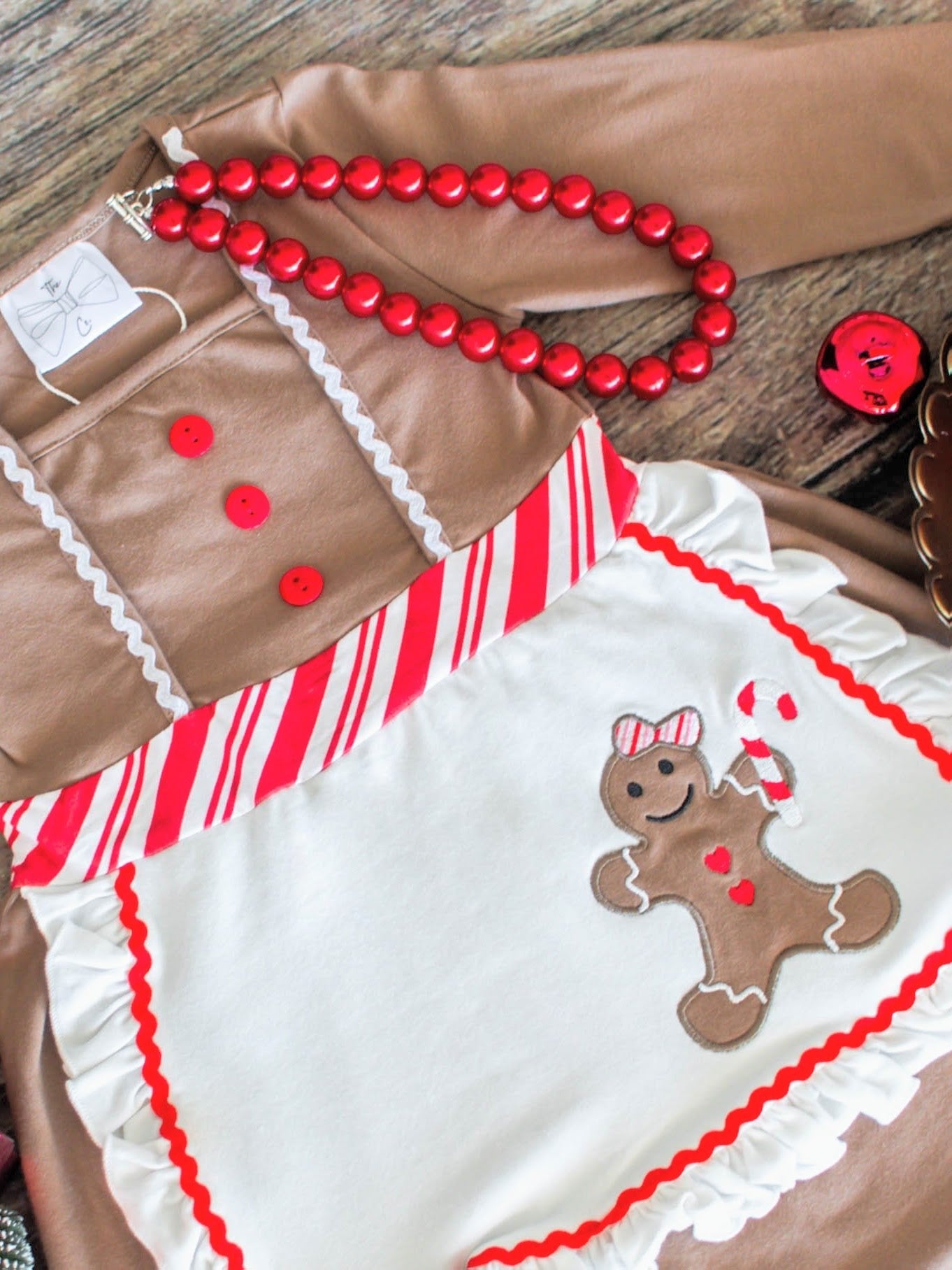 Brown outfit with red buttons and a white apron featuring a gingerbread design on a wooden surface.