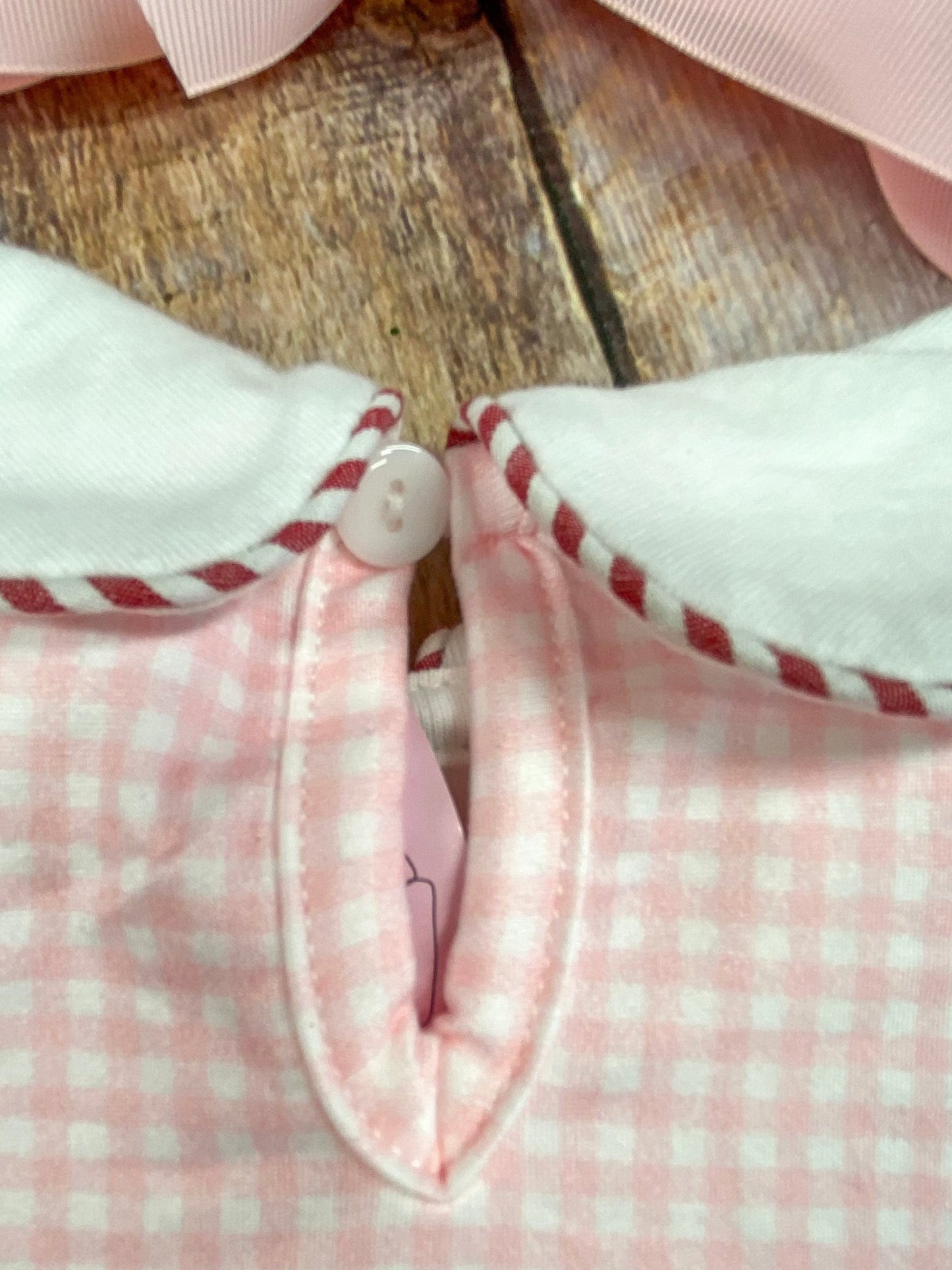 Close-up of a pink and white checkered fabric with a button on a wooden surface