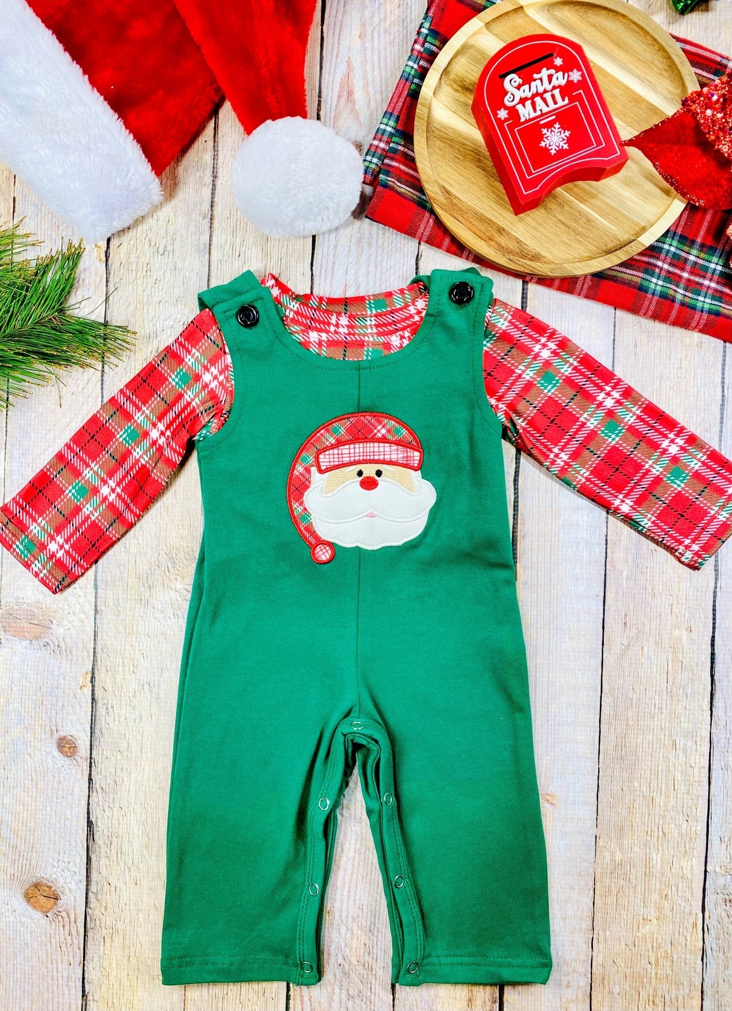 Infant boys’ green Christmas overalls with red plaid long sleeve shirt and Santa face applique on the chest.