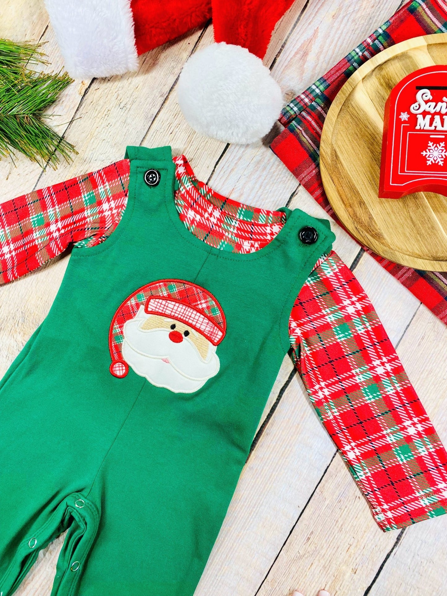 Angled shot of festive baby boy Christmas outfit with plaid sleeves and Santa face detail on the chest.