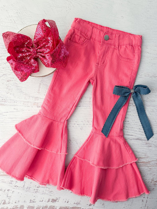 Hot pink frayed double bell bottom jeans displayed next to a pink bow and a blue denim bow. - Alternative view