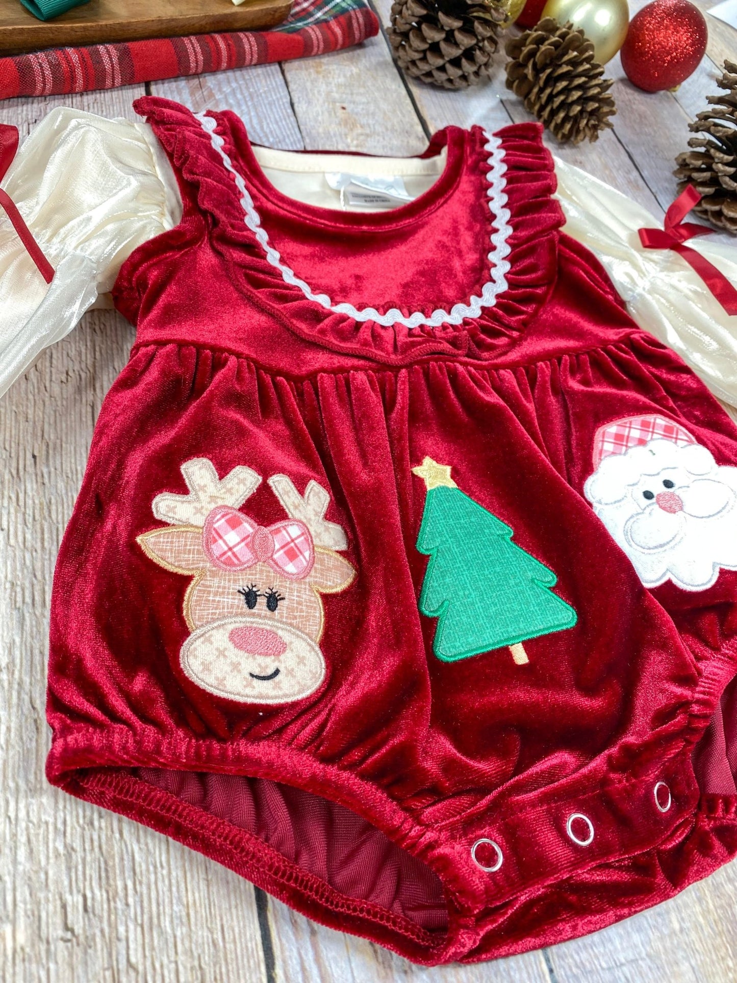Detailed shot of the bottom portion of the romper, showing the gathered red velvet fabric and three small snap buttons at the crotch for easy diaper changes. The Santa and Christmas tree appliqués are visible, highlighting the festive theme
