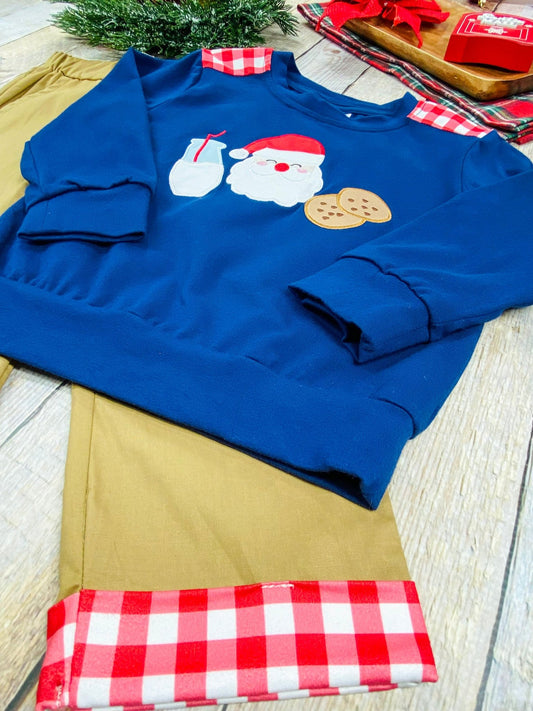 Close-up of a boys’ Christmas outfit featuring a navy blue sweatshirt with Santa, milk, and cookies applique design, paired with tan pants trimmed in red and white buffalo plaid - Alternative view