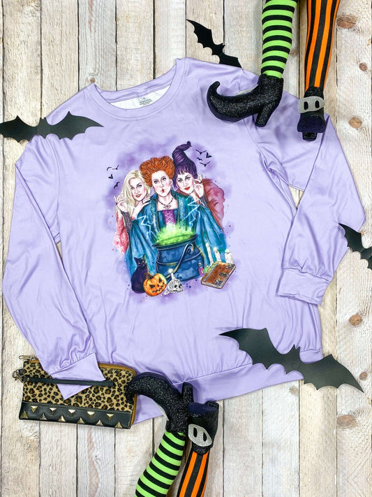 Purple long-sleeve shirt with a graphic of three witches on a wooden surface with Halloween decorations. - Alternative view