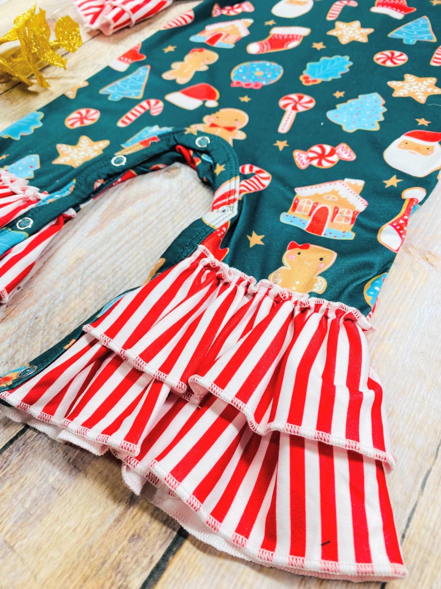 Close-up of baby girls’ romper with Christmas cookie pattern and red striped ruffle cuffs on legs and snaps at bottom.