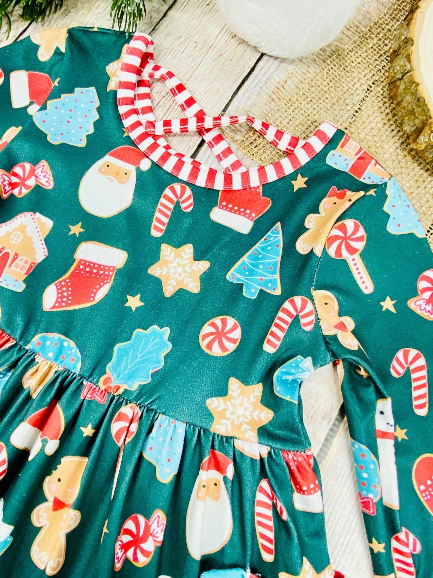 Close-up of girls’ Christmas dress with green background, detailed cookie and holiday icon print, red-and-white striped trim