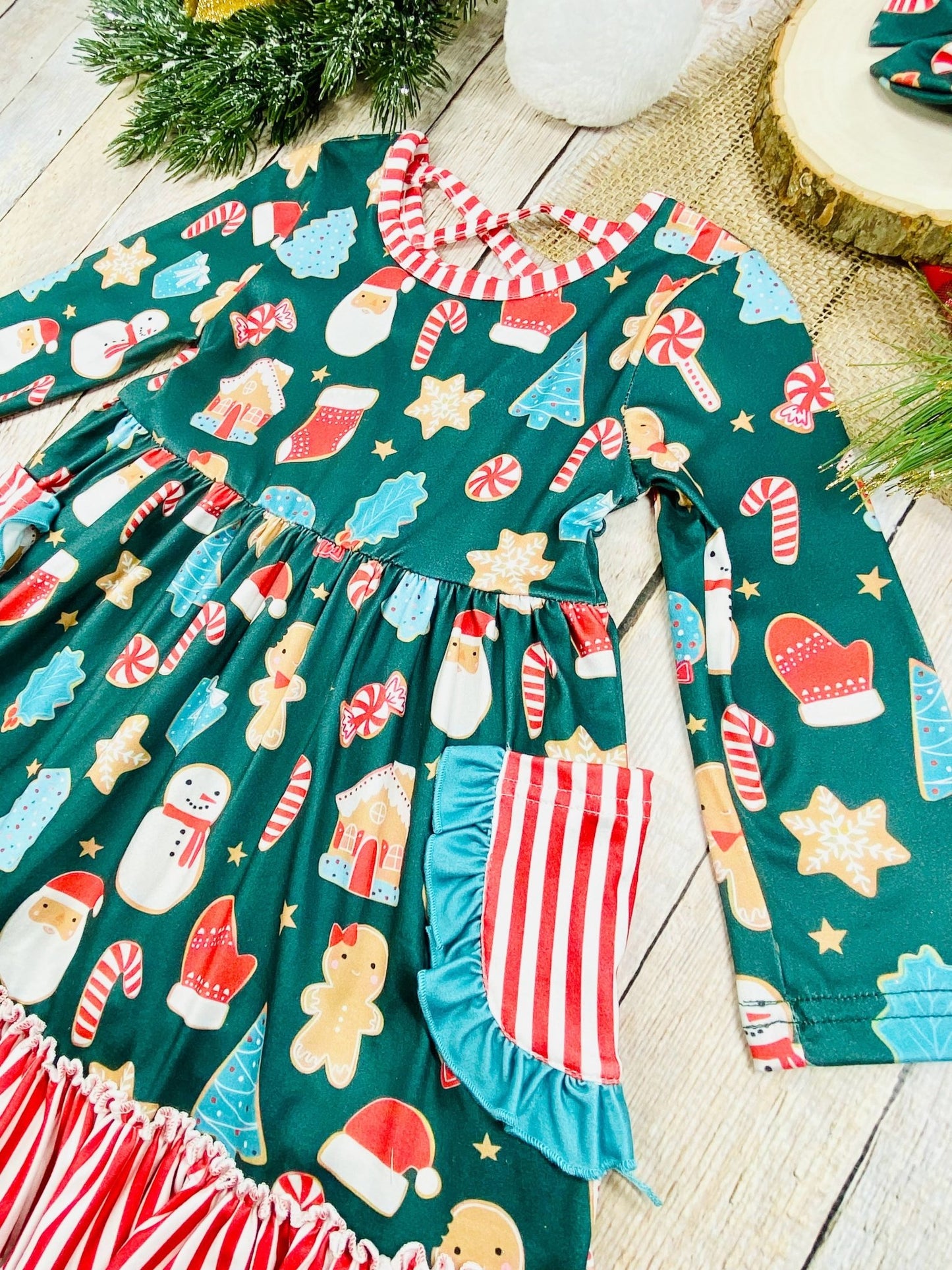 Angled view of holiday twirl dress for girls featuring festive cookie designs, pocket details, and a ruffled striped hem for added texture.