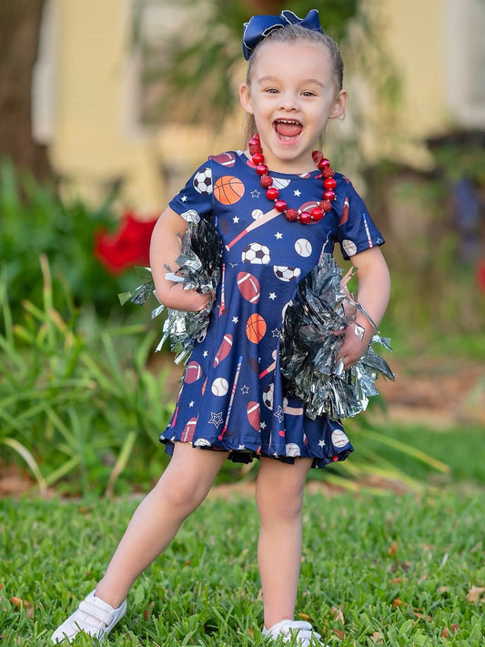 A young girl wearing a navy short sleeve twirl dress with a variety of sports fan pattern - Alternative view