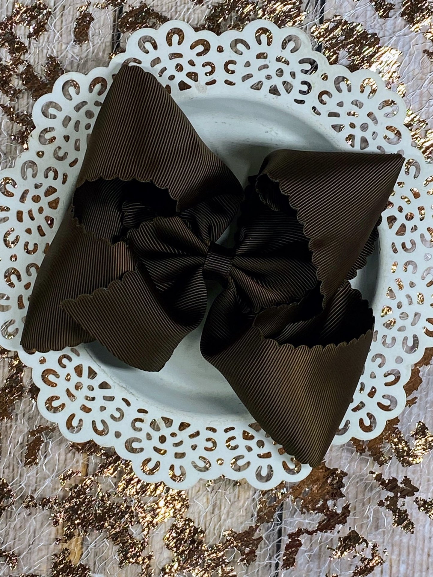Brown hair bow on a decorative white plate with gold glitter background