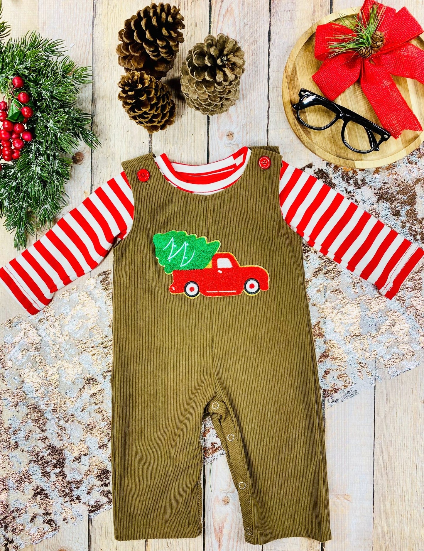 Infant boys’ brown corduroy overalls with red truck and Christmas tree applique, worn over a red-and-white striped shirt.