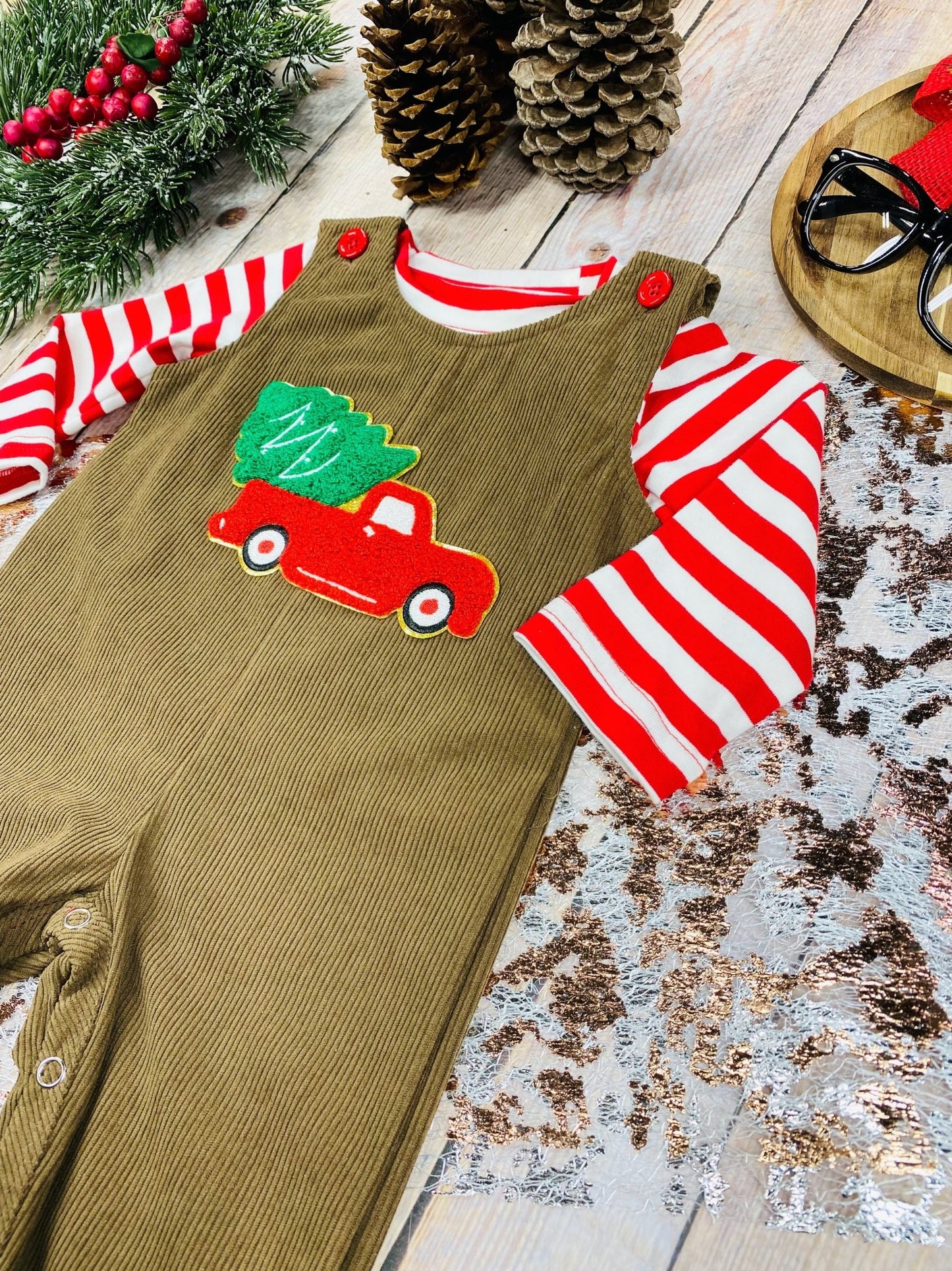 Side view of infant Christmas overalls showing embroidered truck detail and coordinating striped undershirt.