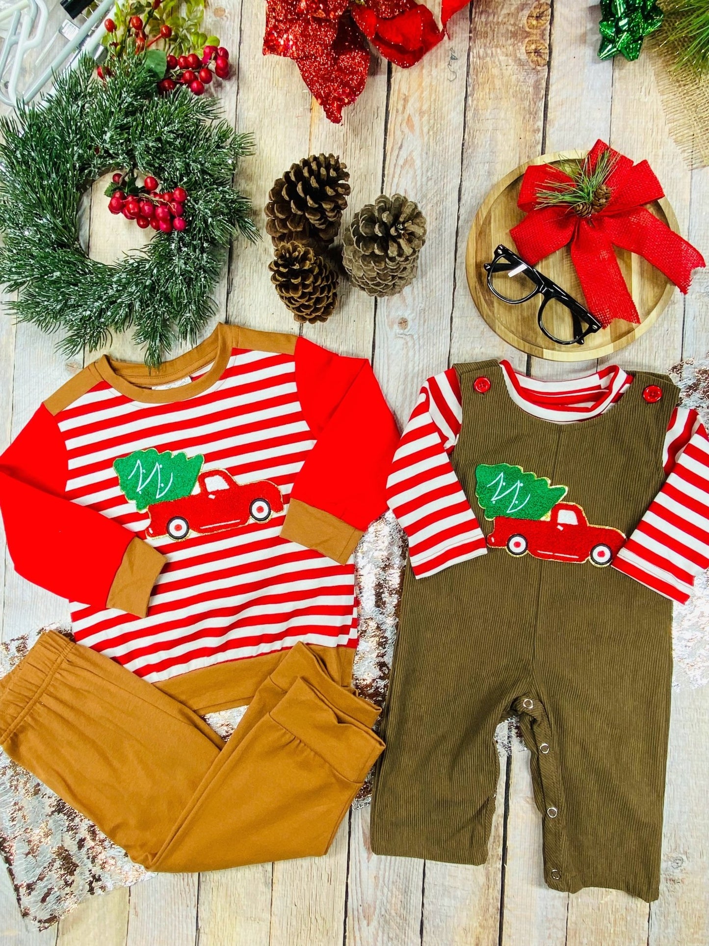 Flat lay of matching boys’ Christmas outfits with red truck and tree appliques both feature red and white stripes on top