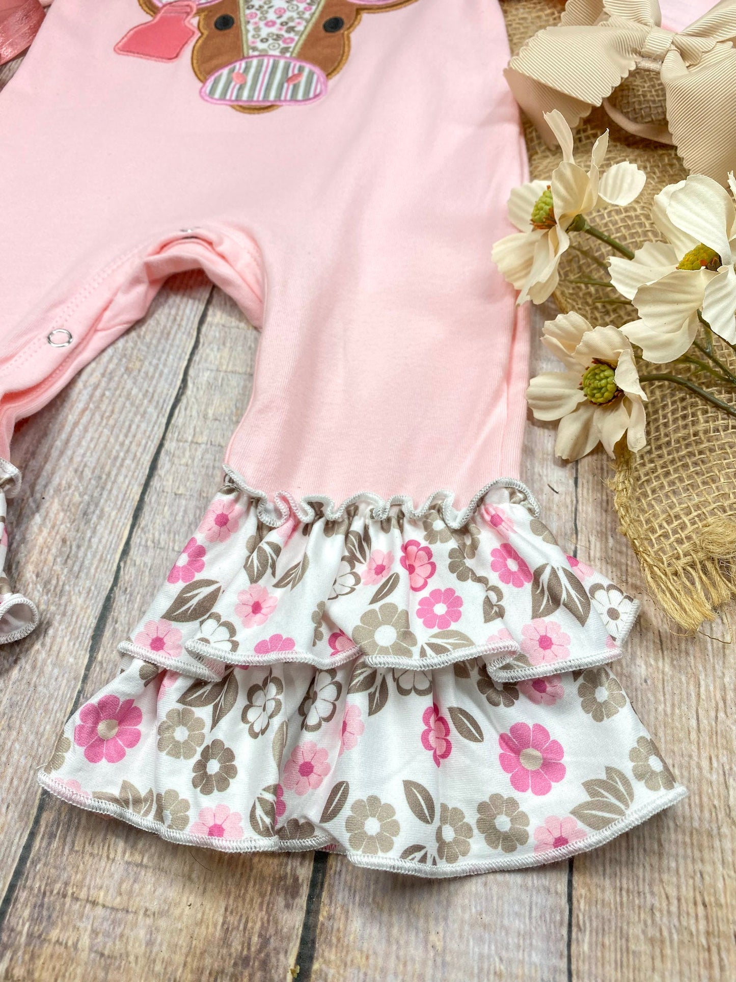baby girl western one-piece with floral cow appliqué and layered floral ruffle leg hems on a wooden background