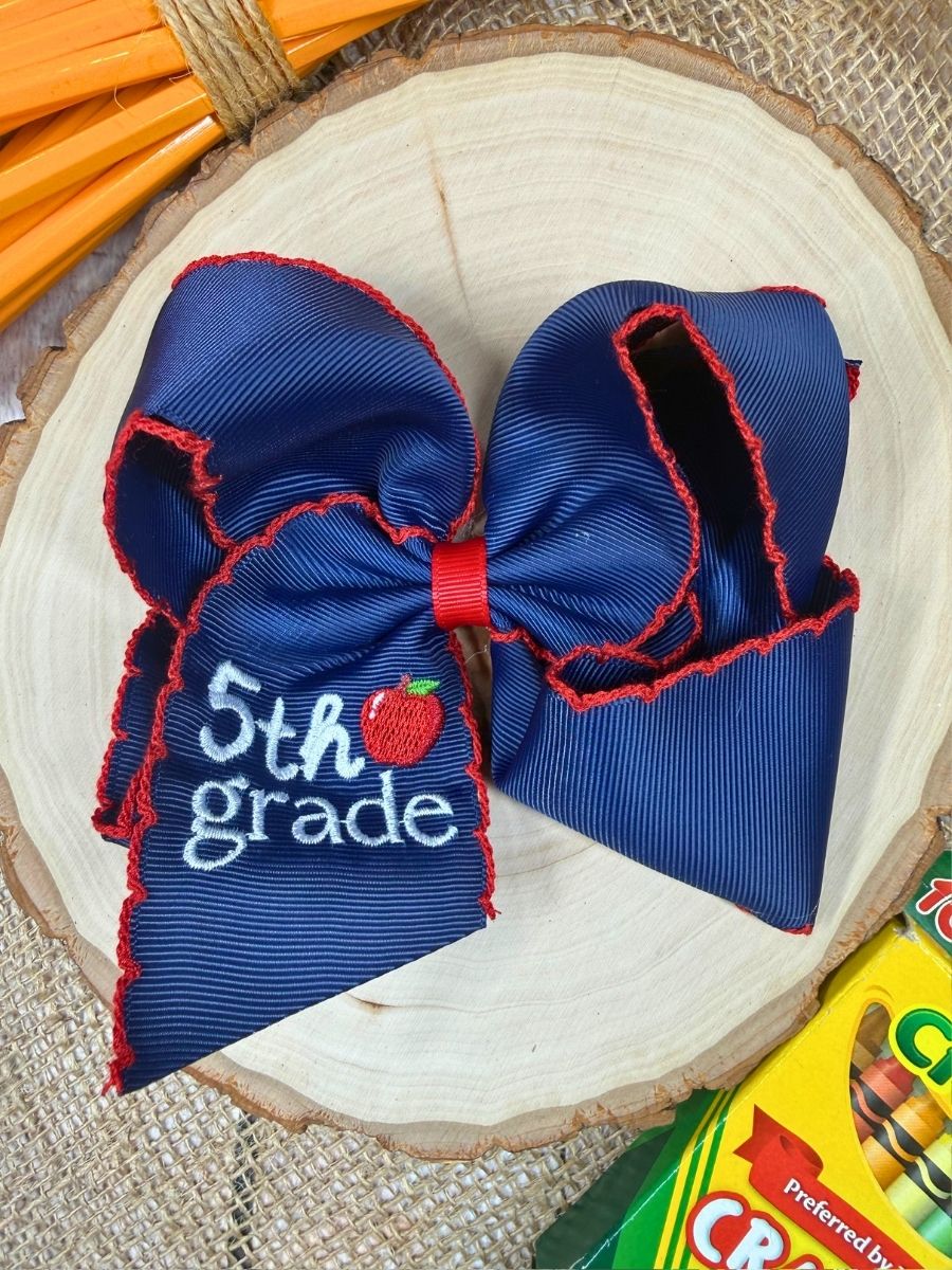 Blue hair bow with '5th grade' and apple design on a wooden surface.