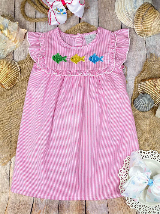 Pink dress with colorful fish appliqués on a wooden background - Alternative view