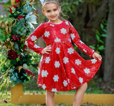 Girl wearing a festive red holiday dress covered in white sequin snowflakes. The dress features long sleeves, a twirl-friendly flared skirt, and a comfortable crew neckline