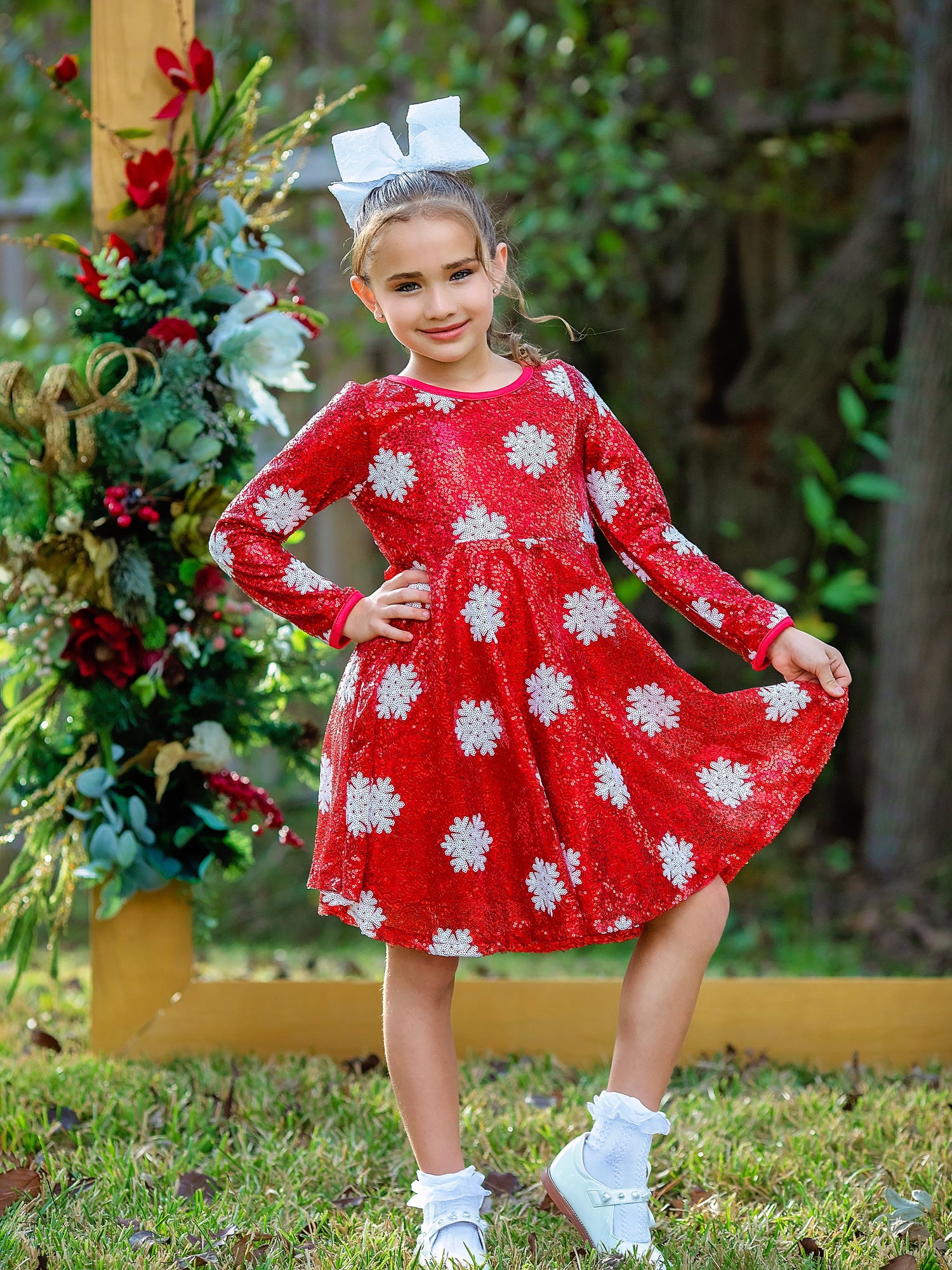 Girl wearing a festive red holiday dress covered in white sequin snowflakes. The dress features long sleeves, a twirl-friendly flared skirt, and a comfortable crew neckline