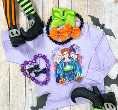 light purple long sleeve featuring a printed scene of hocus pocus witches flat lay styled with decorative fats and hair bows