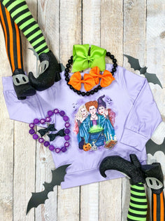 light purple long sleeve featuring a printed scene of hocus pocus witches flat lay styled with decorative fats and hair bows