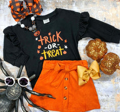 black long sleeve with text saying "trick or treat" in orange and yellow colors with a orange skirt tied with bow and buttons down middle flat lay styled with halloween decorations and hair bows