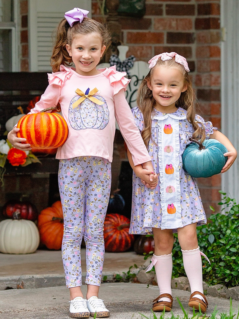 Lavender fall matching outfits on two little girls holding hands and pumpkins.