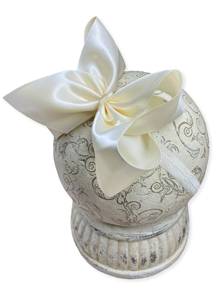 Decorative urn with intricate patterns and a large cream-colored bow on a white background