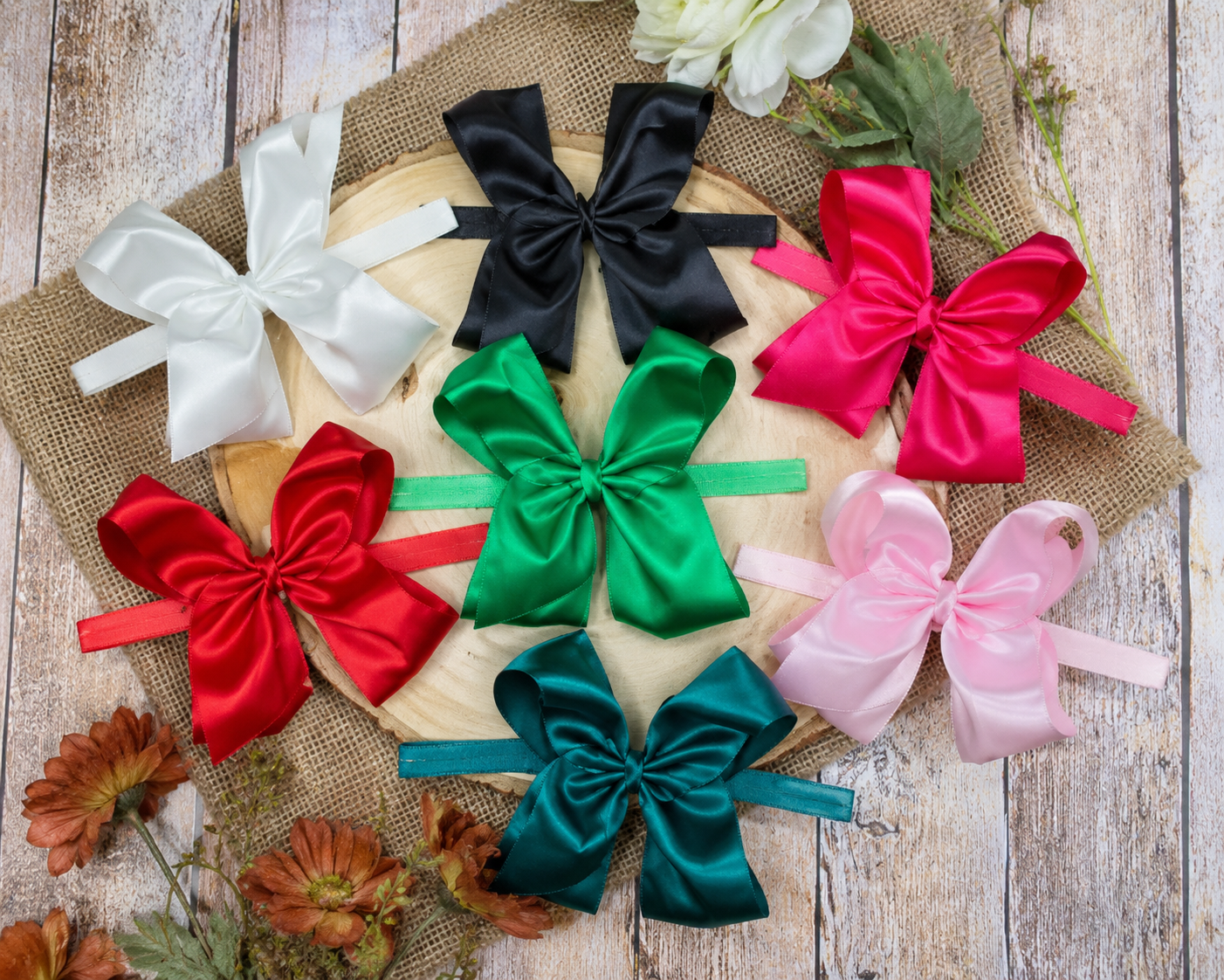 4.5 inch classic satin headbands in hunter green, emerald, white, black, pink, on a wooden background 