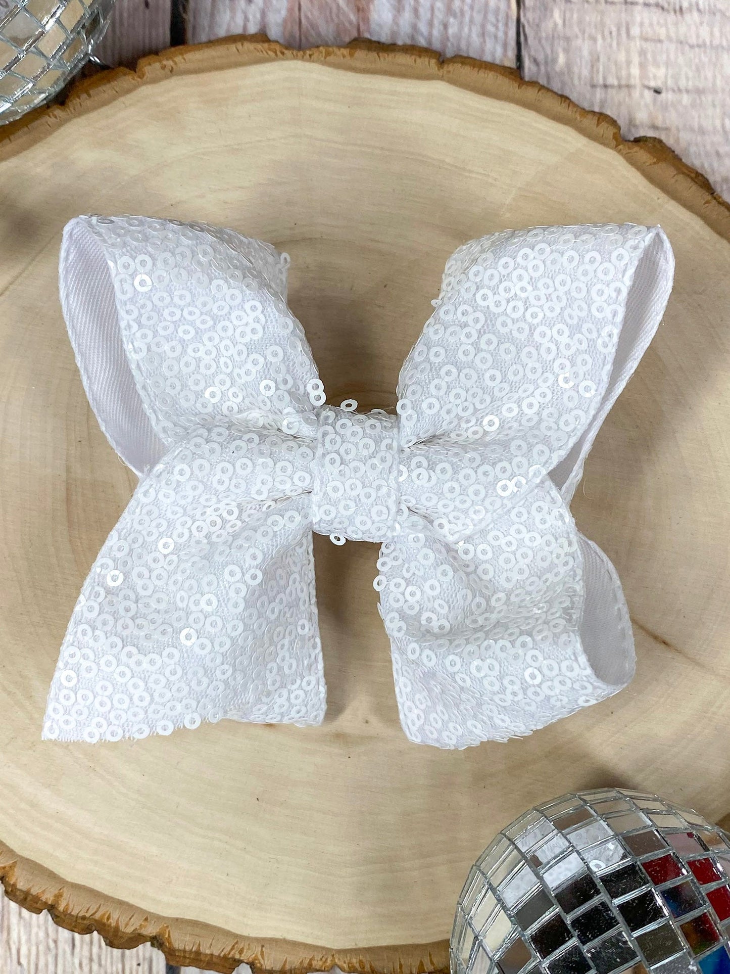 White sequin bow on a wooden surface with decorative items.