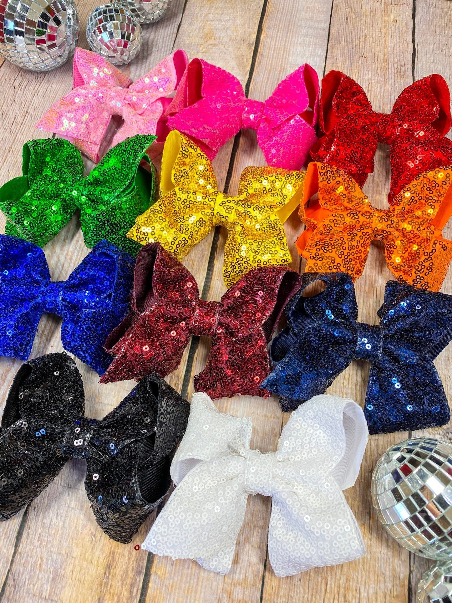 Colorful glittery bows on a wooden surface with disco balls around.