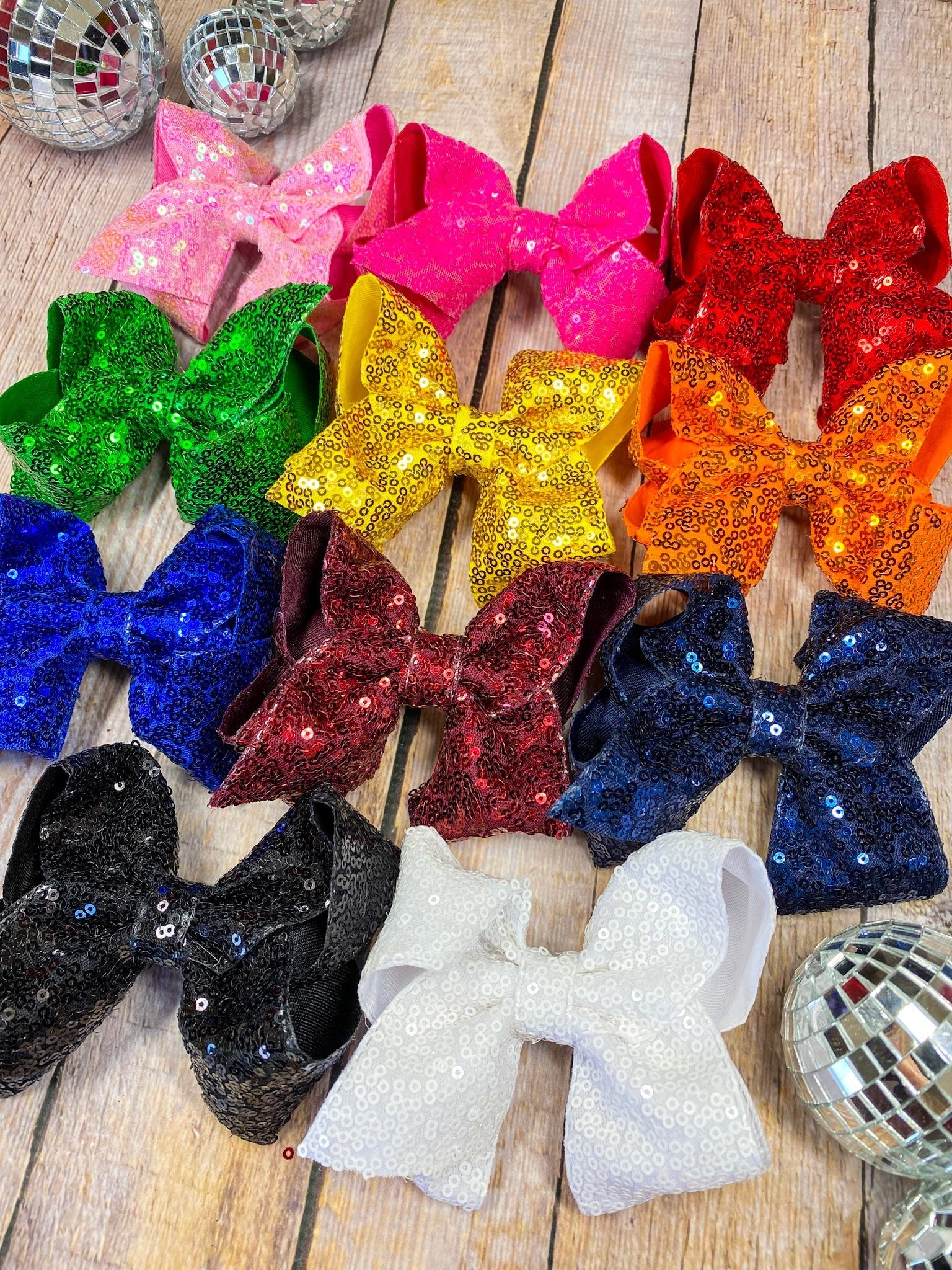 Colorful glittery bows on a wooden surface with disco balls around.