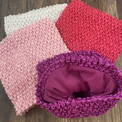 Four stretchy crochet tutu tops in white, light pink, hot pink, and fuchsia, displayed on a wooden surface. The fuchsia one is turned inside out, showing a smooth fabric lining