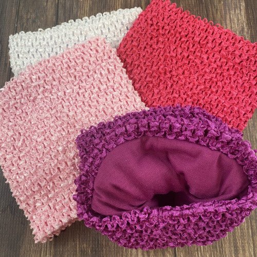 Four stretchy crochet tutu tops in white, light pink, hot pink, and fuchsia, displayed on a wooden surface. The fuchsia one is turned inside out, showing a smooth fabric lining - Alternative view