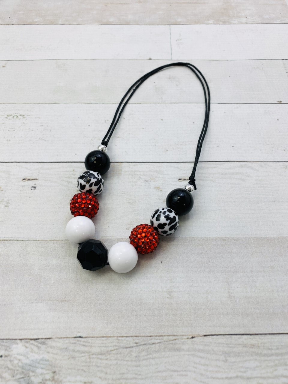 Adjustable wax-coated rope chunky bead necklace with cow print, red rhinestone, solid black, and solid white chunky beads.