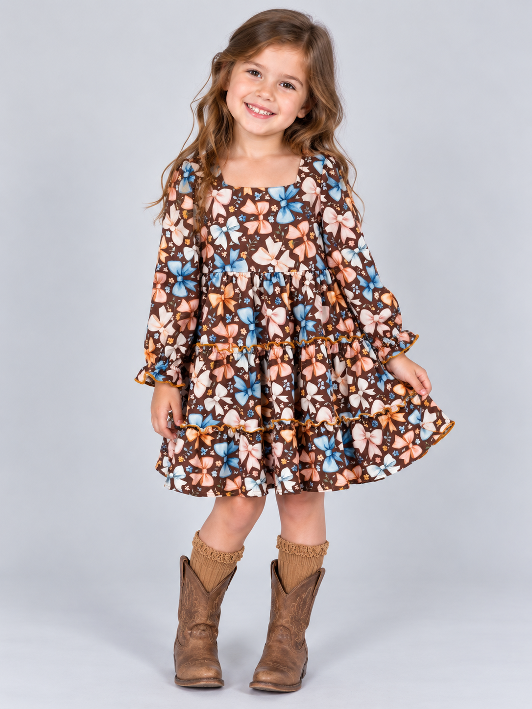 model wearing Girls brown bow print tiered dress with long sleeves and ruffle details
